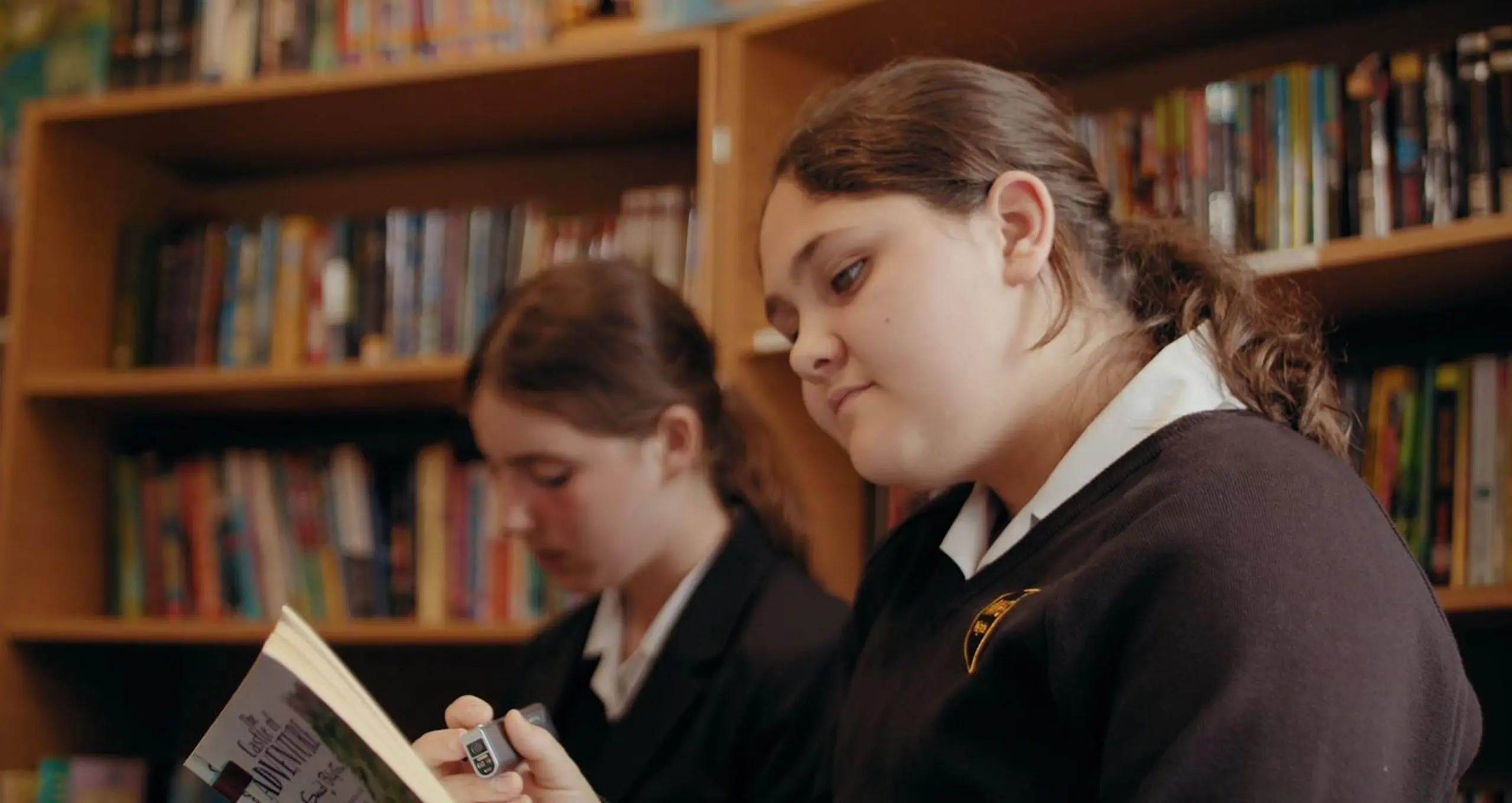 Two female students in school uniform reading books together in the Moon Hall School library