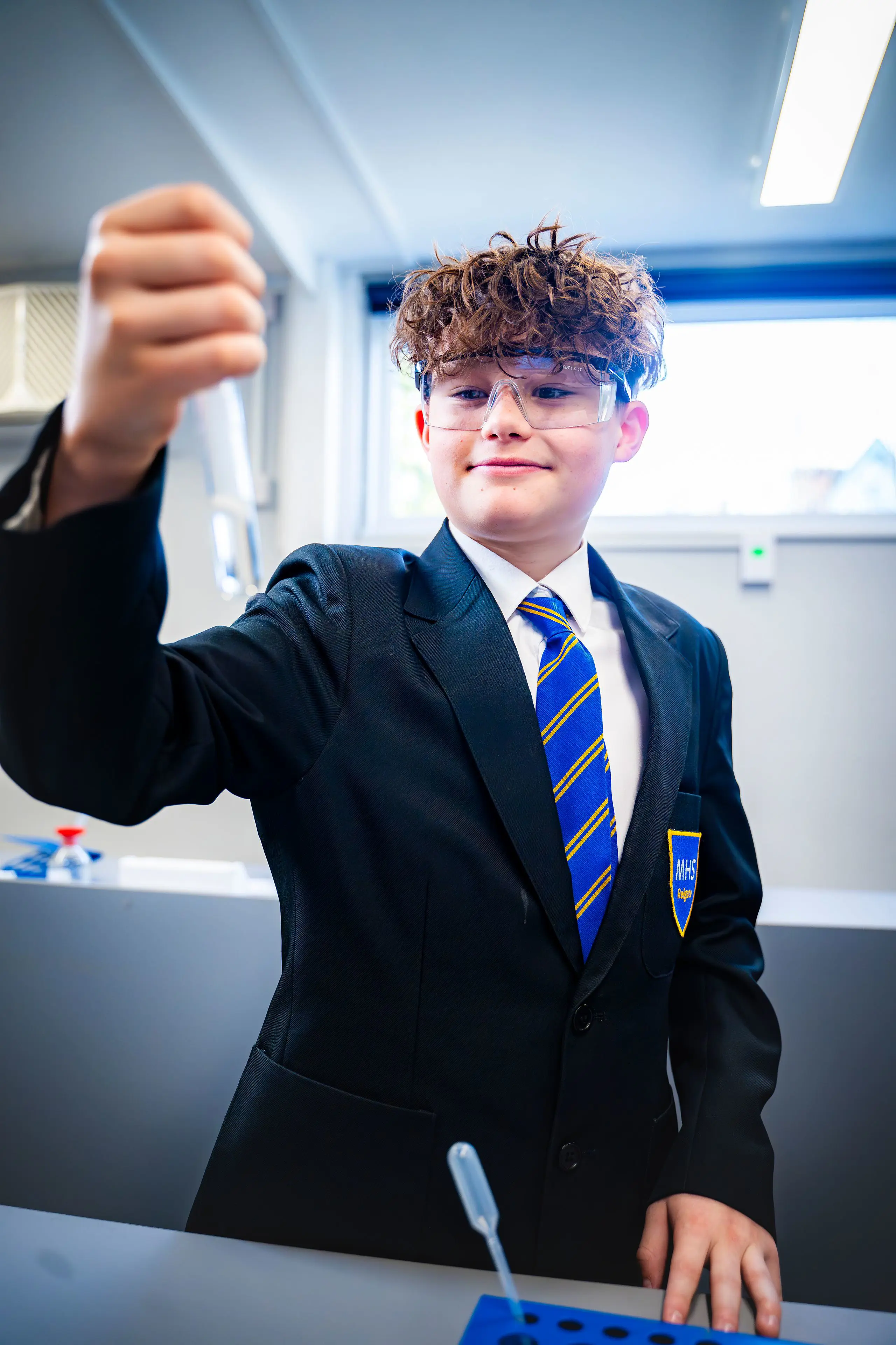 Male pupil in school blazer and tie holding up a test tube in a science lab