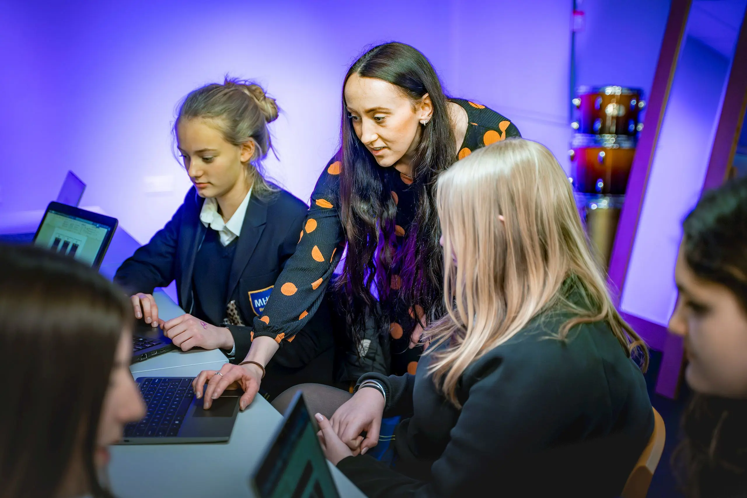 Female teacher guiding two students as they work on laptops in a modern music classroom