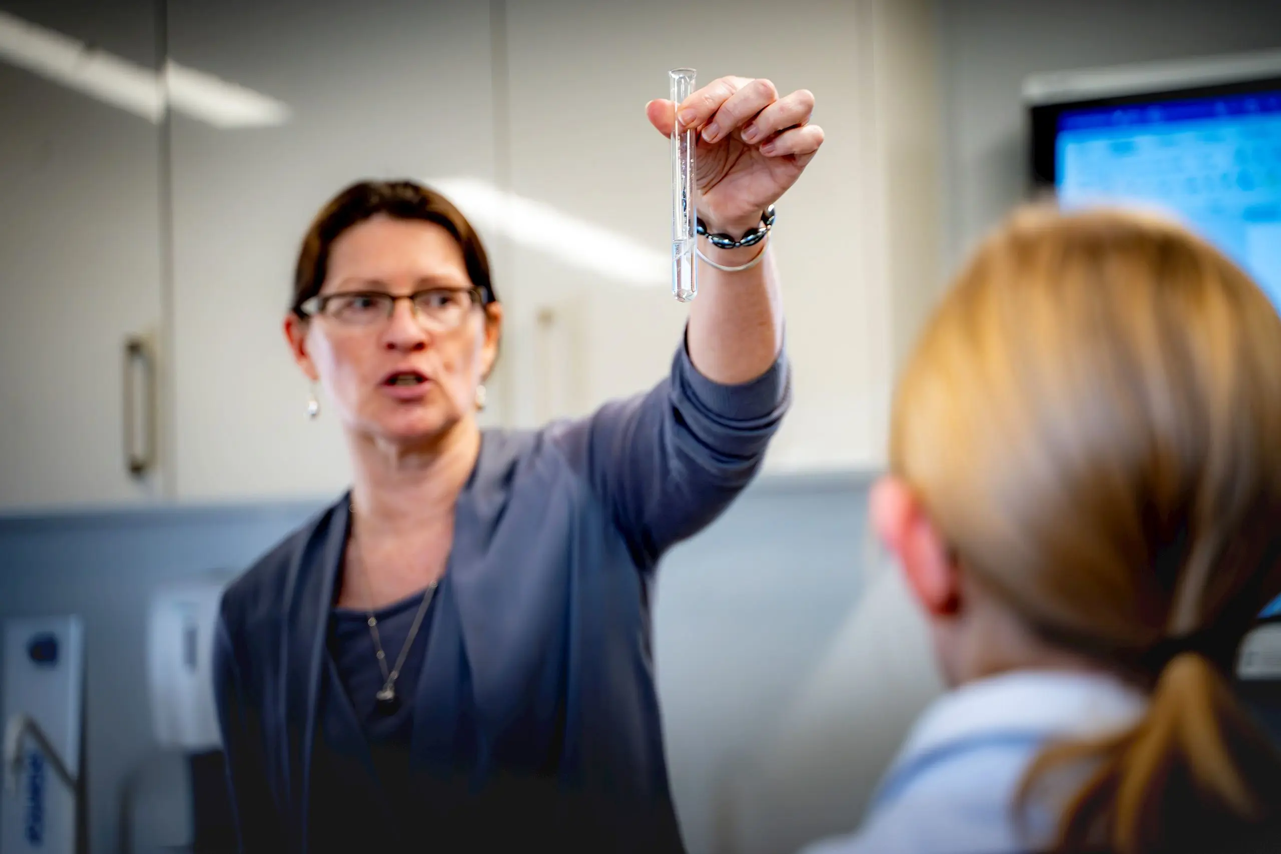 Female teacher holding up a test tube while explaining a practical science concept to a student