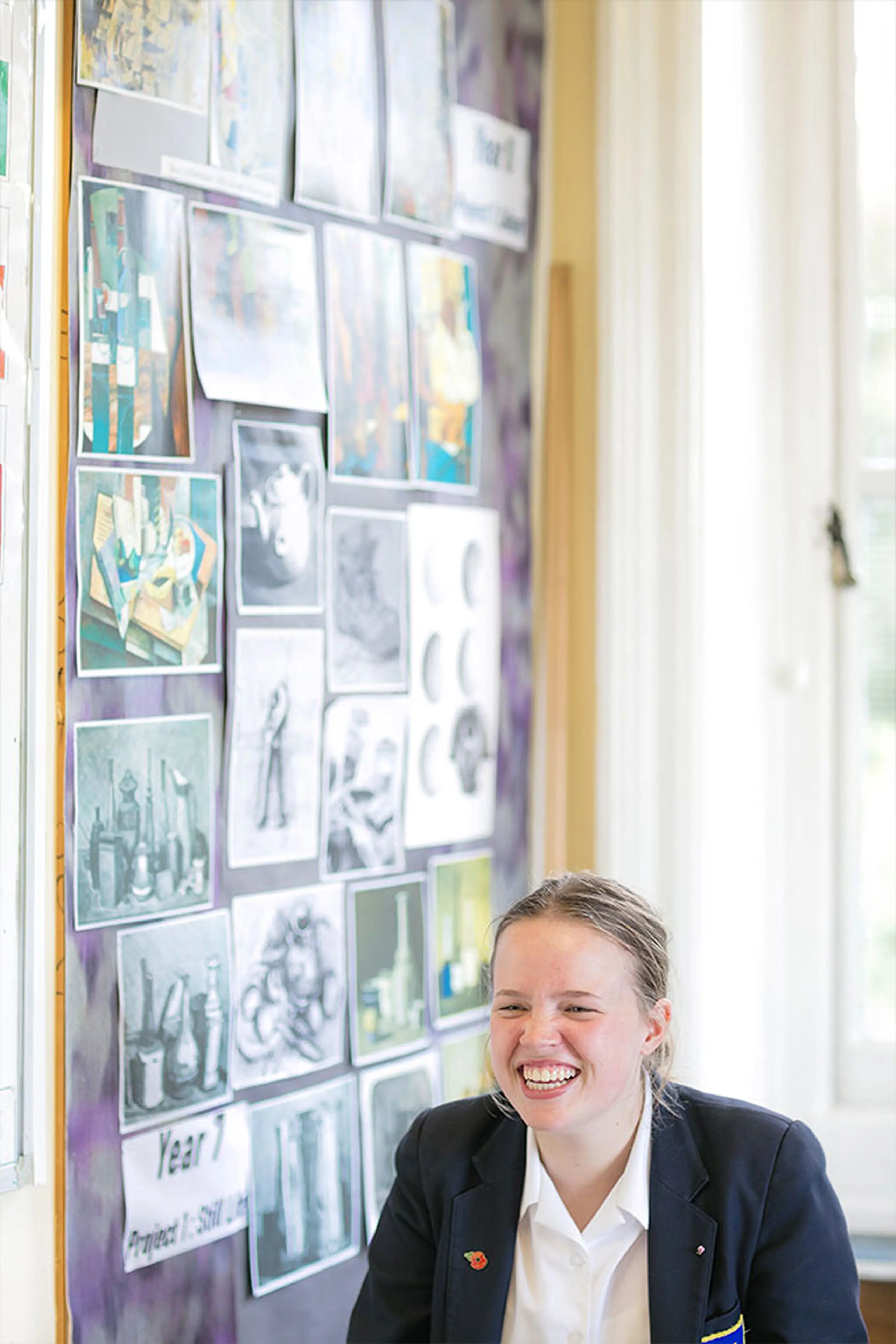Smiling student sitting near a wall display featuring student artwork and photos