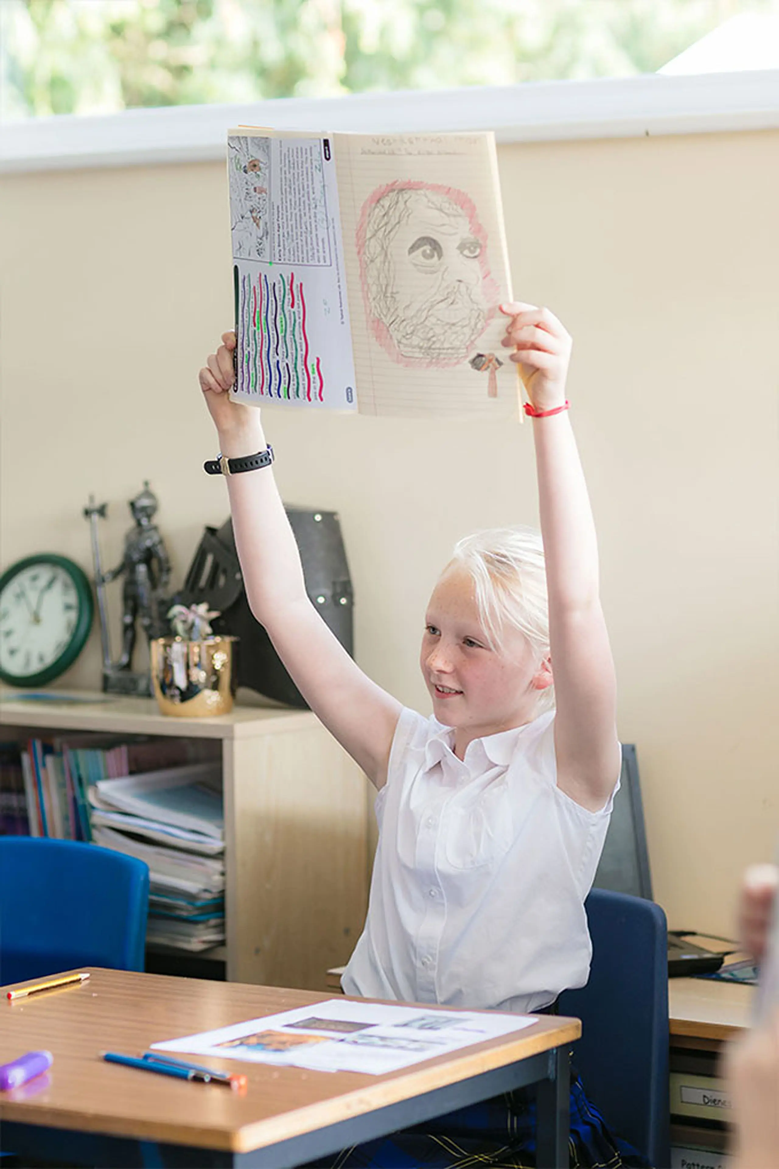 Young pupil proudly holding up artwork in a classroom