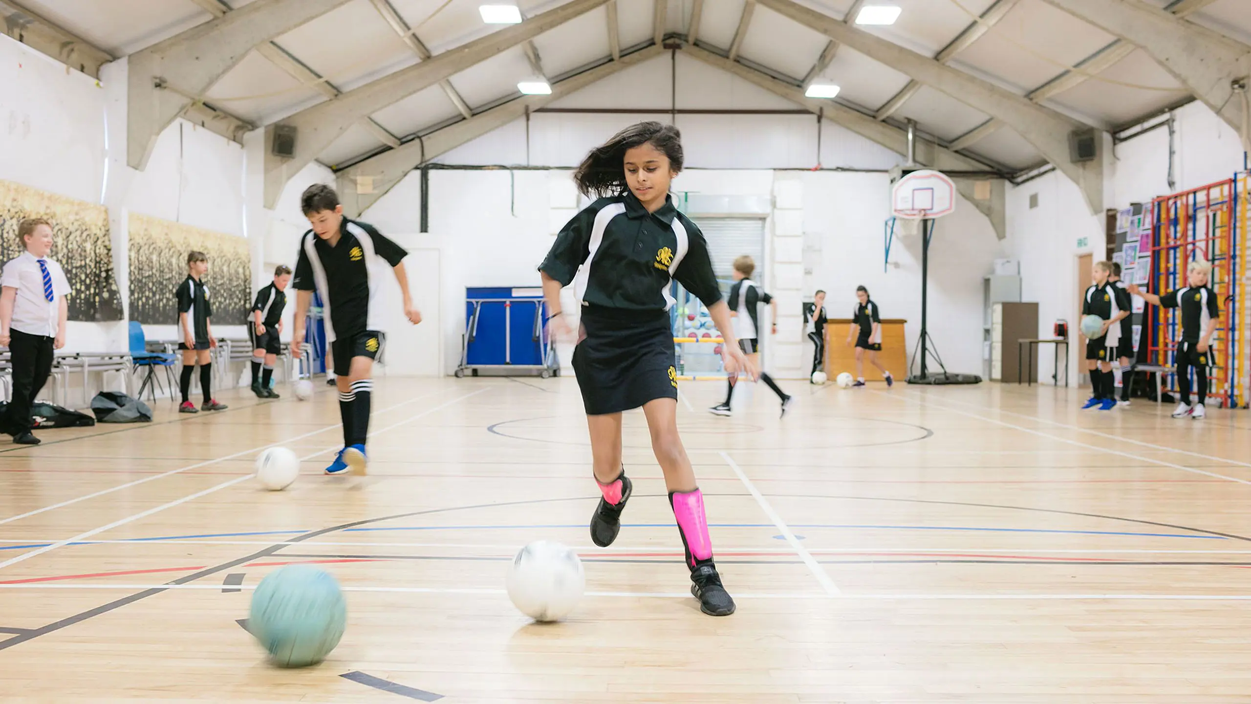 Pupils playing football inside a large school sports hall